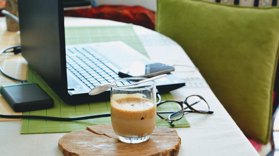 A macbook, cup of coffee, glasses on a table