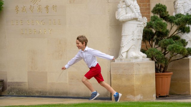 A boy in bright red shorts runs outside the College library