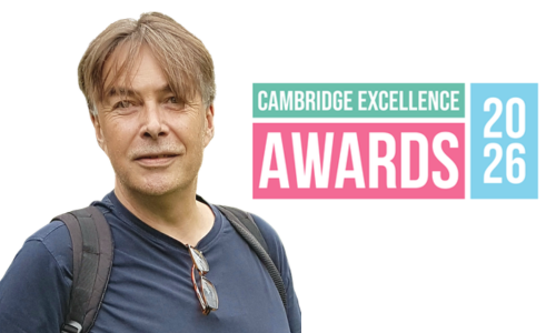 Head and shoulders portrait of a person wearing a navy T-shirt and backpack, with glasses hanging from the shirt collar, standing against a white background. To the right is a colourful graphic reading 'Cambridge Excellence Awards 2026' in teal, pink, and light blue.