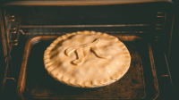 A homemade pie with a crimped crust and the symbol for pi added on the top bakes on a tray inside an oven.